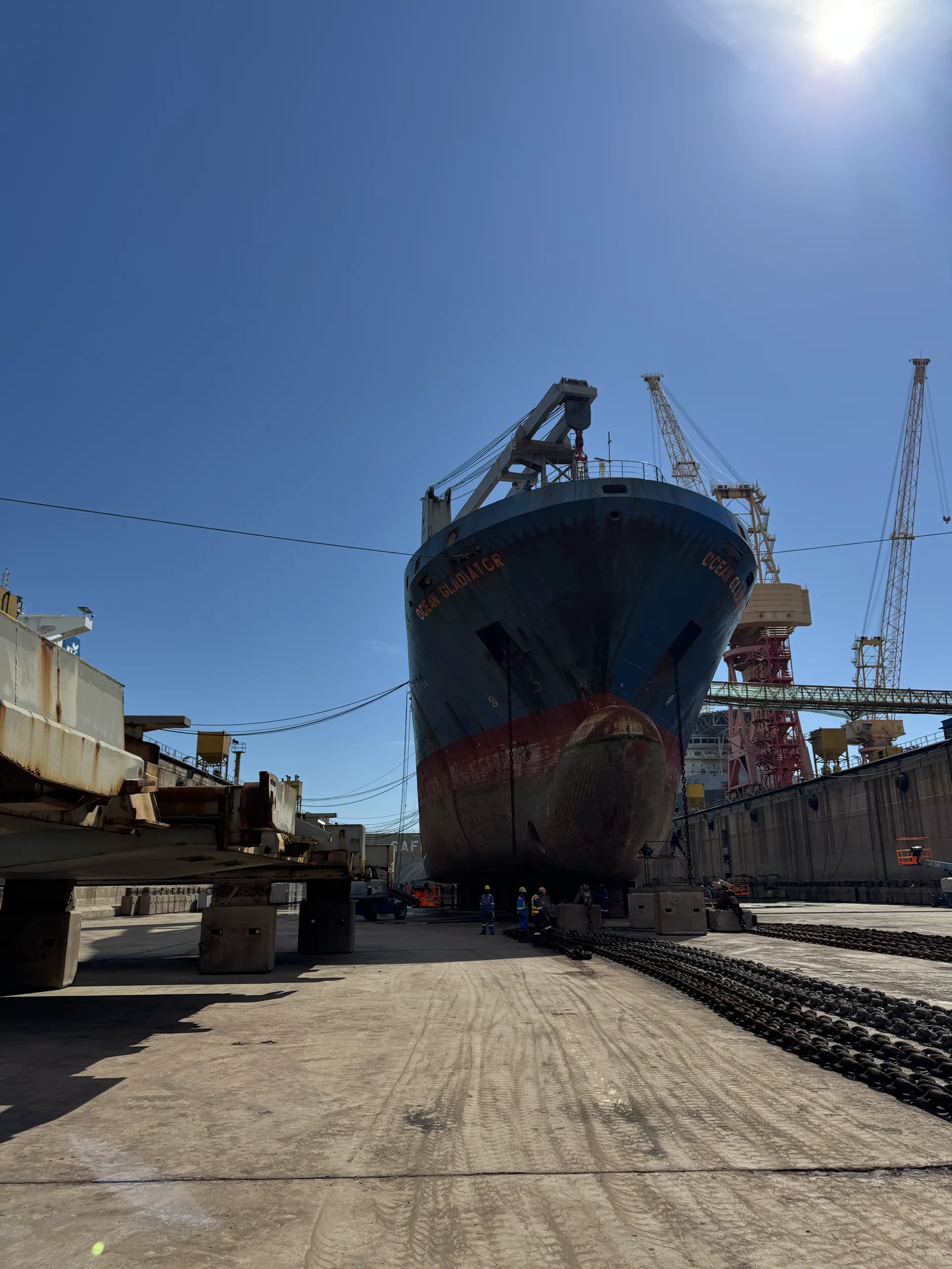 Cargo vessel in drydock with shipyard cranes behind